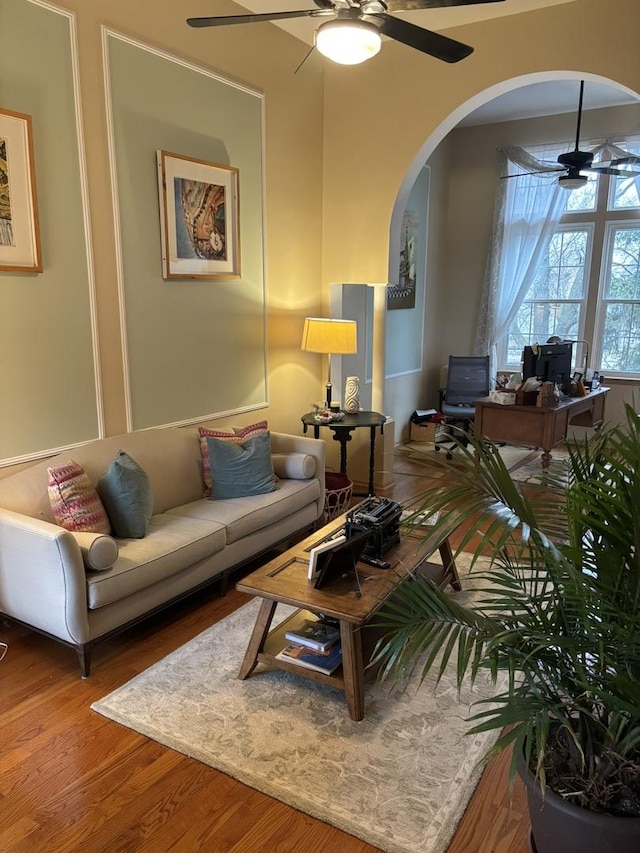 living room with ceiling fan, arched walkways, and wood finished floors