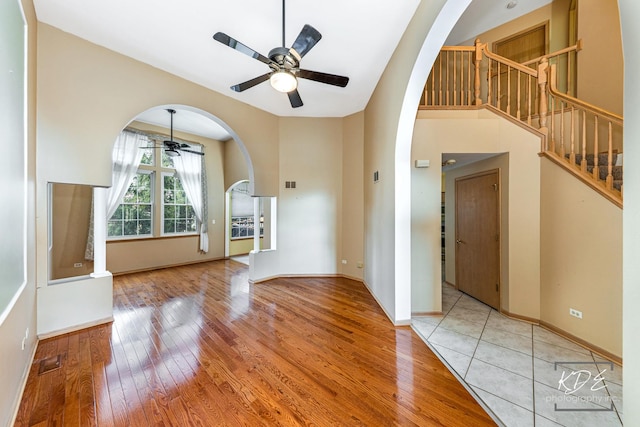 unfurnished living room featuring a ceiling fan, wood-type flooring, baseboards, and stairs