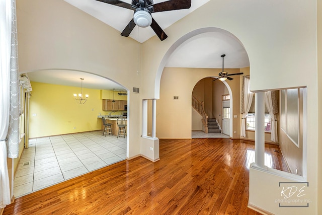 unfurnished room featuring visible vents, arched walkways, wood finished floors, stairs, and ceiling fan with notable chandelier