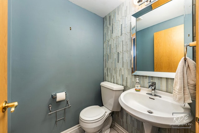 bathroom featuring tasteful backsplash, a sink, toilet, and baseboards