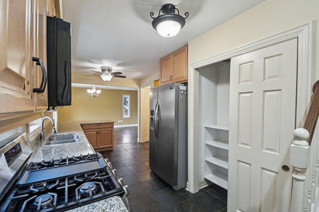 kitchen featuring ceiling fan with notable chandelier, a sink, baseboards, appliances with stainless steel finishes, and light stone countertops