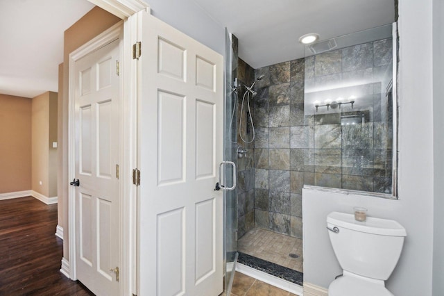 full bathroom with toilet, baseboards, a tile shower, and wood finished floors