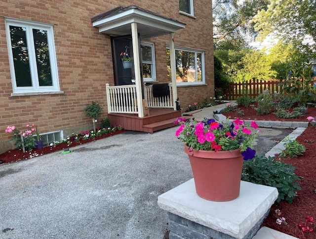 doorway to property with a porch, brick siding, and fence