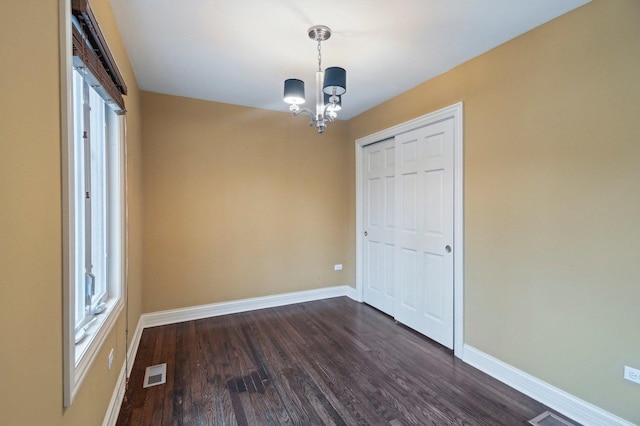 unfurnished room with dark wood-style flooring, an inviting chandelier, visible vents, and baseboards