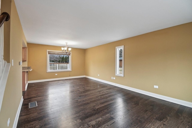 empty room with dark wood-style flooring, visible vents, baseboards, and an inviting chandelier