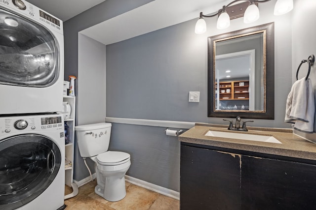 bathroom featuring toilet, vanity, baseboards, and stacked washer and clothes dryer