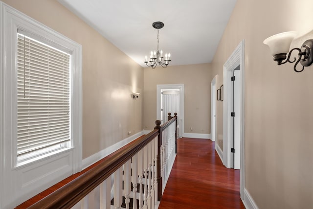 hallway featuring dark wood-style floors, baseboards, an inviting chandelier, and an upstairs landing