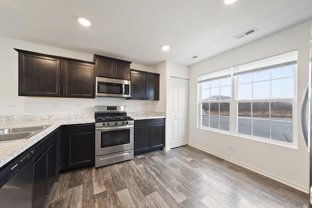 kitchen featuring stainless steel appliances, a sink, visible vents, light countertops, and dark wood-style floors