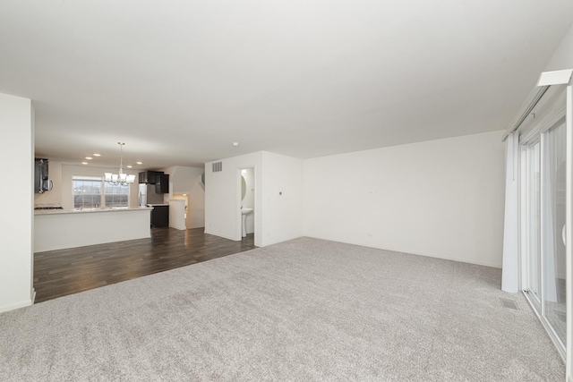 unfurnished living room with dark carpet, visible vents, and a notable chandelier