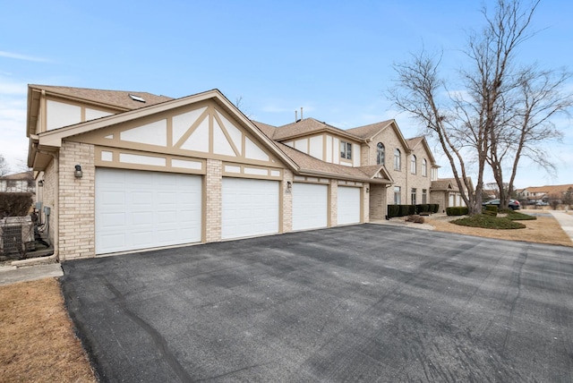 view of front facade featuring a shingled roof, stucco siding, aphalt driveway, an attached garage, and brick siding