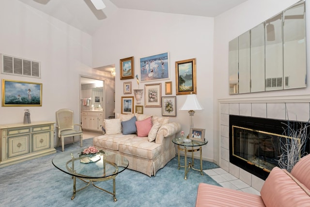 living area with high vaulted ceiling, a tiled fireplace, visible vents, and a ceiling fan