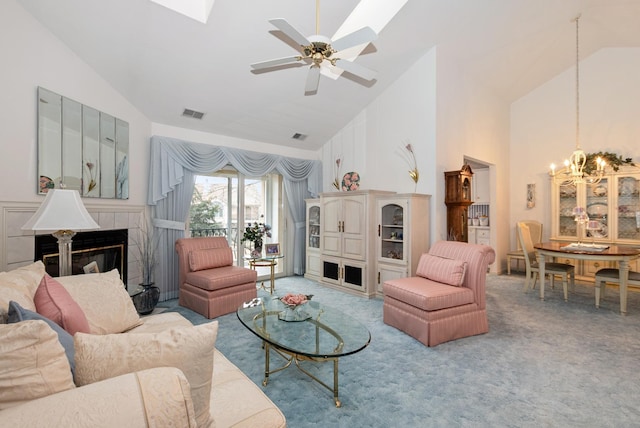 carpeted living area featuring ceiling fan with notable chandelier, high vaulted ceiling, a tiled fireplace, and visible vents