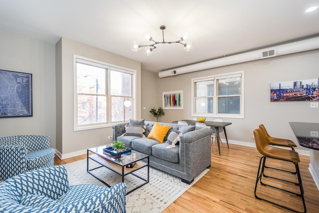 living room with an inviting chandelier, visible vents, baseboards, and light wood finished floors