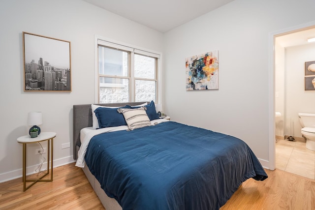 bedroom with baseboards, light wood-style floors, and ensuite bath