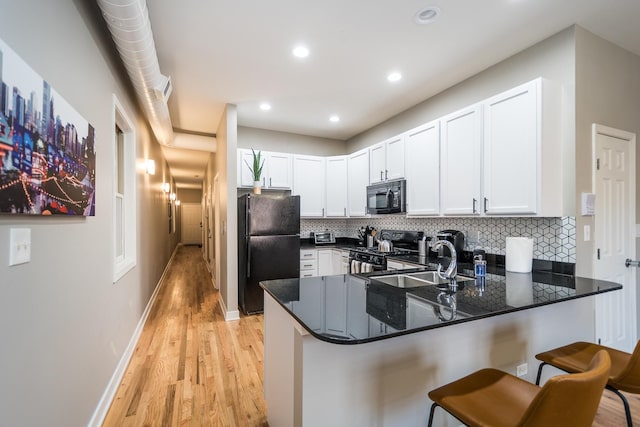 kitchen featuring a peninsula, a sink, black appliances, white cabinetry, and backsplash