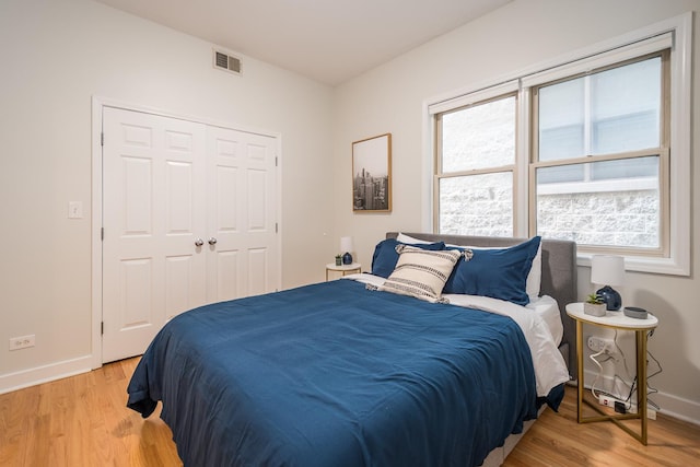 bedroom featuring light wood-style flooring, visible vents, baseboards, and a closet