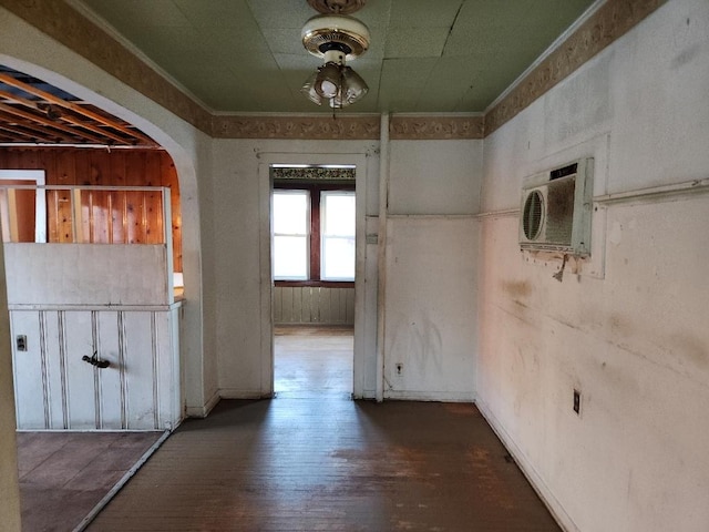 interior space with a wall mounted AC, arched walkways, wood finished floors, and ornamental molding