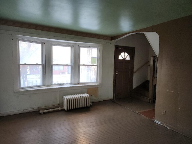 foyer entrance with arched walkways, stairway, and radiator