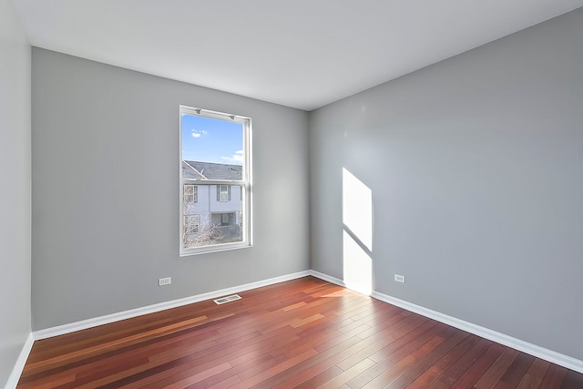 empty room featuring hardwood / wood-style floors, visible vents, and baseboards