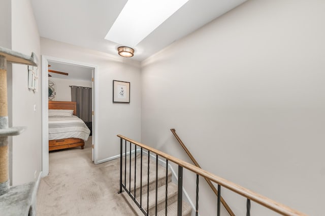 hall with a skylight, an upstairs landing, baseboards, and light carpet