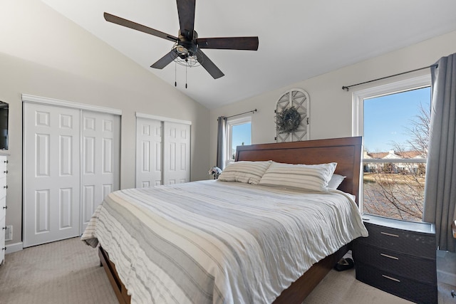 bedroom featuring multiple closets, light colored carpet, lofted ceiling, and a ceiling fan