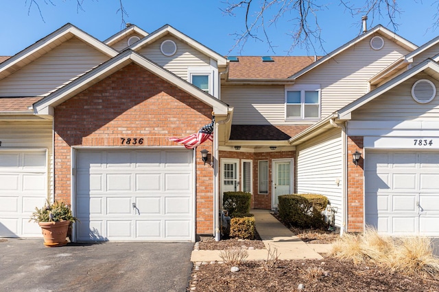 townhome / multi-family property with an attached garage, brick siding, driveway, and a shingled roof