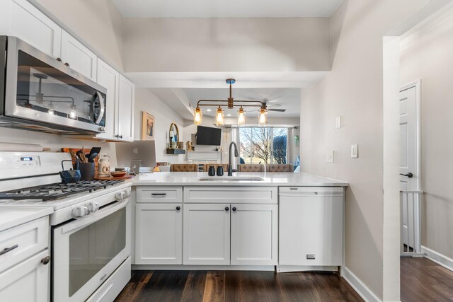 kitchen featuring a sink, dark wood finished floors, white appliances, a peninsula, and white cabinets