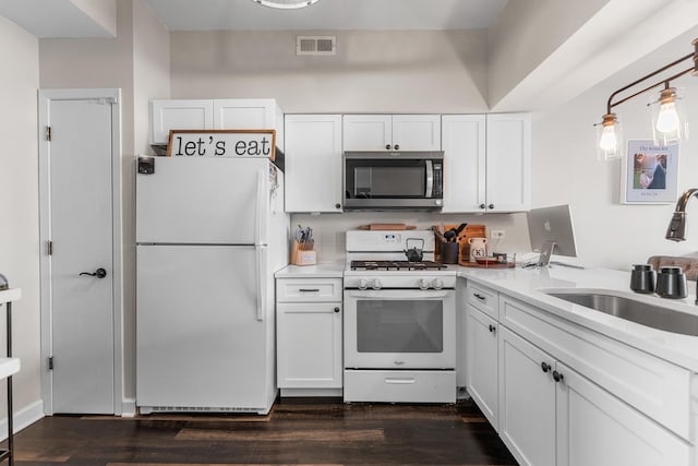 kitchen with white appliances, visible vents, dark wood finished floors, a sink, and white cabinets