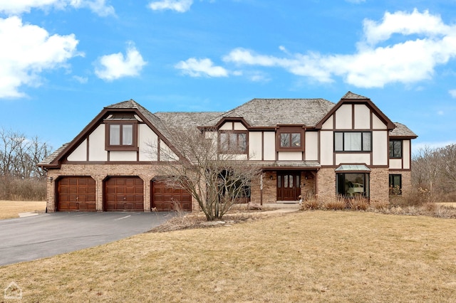 english style home featuring an attached garage, stucco siding, a front lawn, aphalt driveway, and brick siding