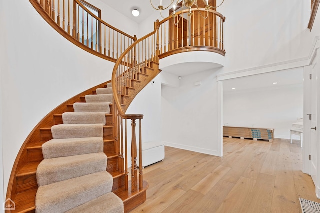 staircase with hardwood / wood-style flooring, a high ceiling, baseboards, and visible vents