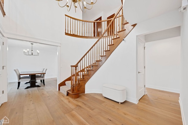 stairs with hardwood / wood-style floors, an inviting chandelier, a high ceiling, and baseboards