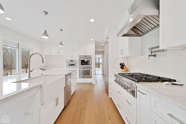 kitchen with extractor fan, pendant lighting, stainless steel appliances, light wood-style floors, and white cabinetry