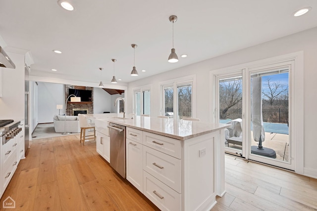 kitchen with light wood finished floors, a brick fireplace, open floor plan, light stone counters, and white cabinetry