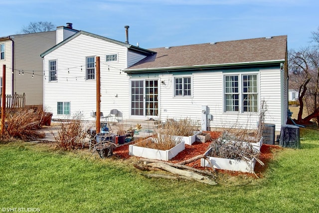 back of property featuring a yard, a patio area, roof with shingles, and a vegetable garden