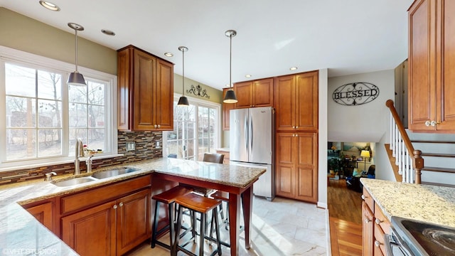 kitchen with light stone countertops, backsplash, a sink, and freestanding refrigerator