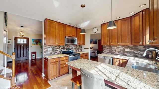 kitchen featuring brown cabinets, decorative backsplash, appliances with stainless steel finishes, a sink, and light stone countertops