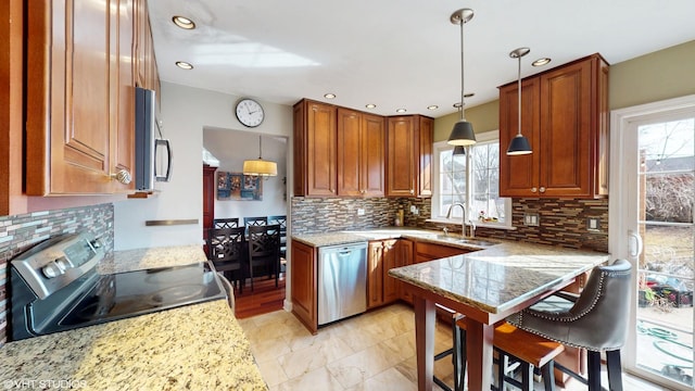 kitchen with brown cabinets, stainless steel appliances, a sink, and decorative light fixtures