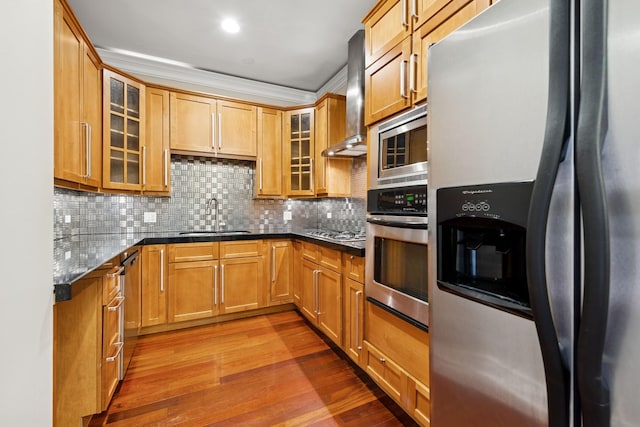 kitchen featuring wood finished floors, a sink, wall chimney range hood, appliances with stainless steel finishes, and backsplash