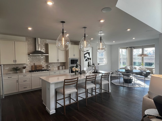 kitchen featuring gas stovetop, a kitchen breakfast bar, light countertops, wall chimney exhaust hood, and stainless steel microwave