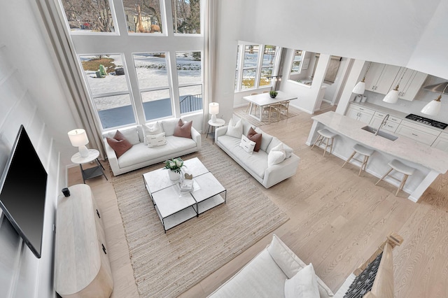 living area with light wood-type flooring, a towering ceiling, and baseboards