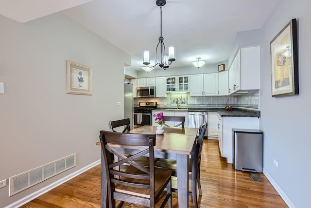 dining space featuring light wood-type flooring, visible vents, a notable chandelier, and baseboards