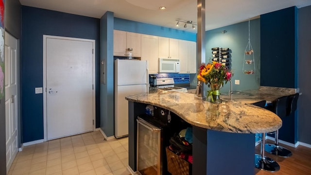 kitchen with wine cooler, light stone counters, white appliances, white cabinets, and tasteful backsplash