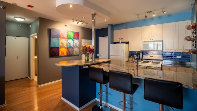 kitchen with stone counters, light wood finished floors, a breakfast bar area, tasteful backsplash, and white appliances