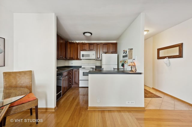 kitchen featuring light wood-type flooring, dark countertops, white appliances, and baseboards