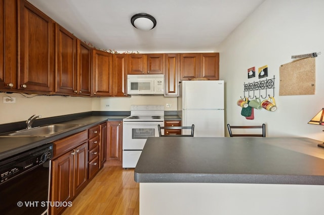 kitchen featuring white appliances, a sink, light wood-type flooring, brown cabinets, and dark countertops