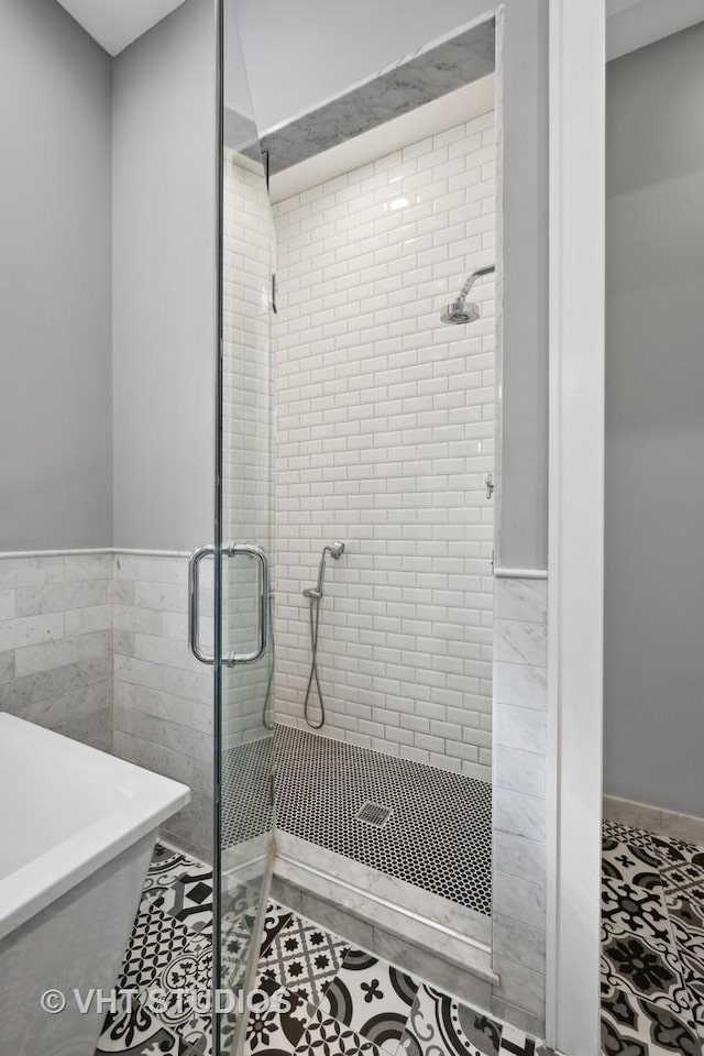 bathroom with a shower stall, a soaking tub, tile walls, and tile patterned floors