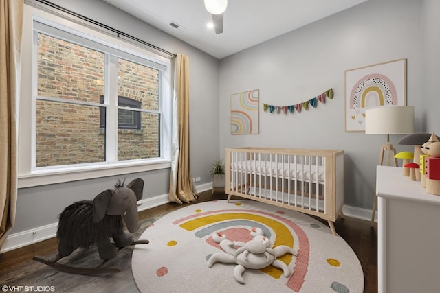 bedroom with visible vents, multiple windows, a nursery area, and wood finished floors