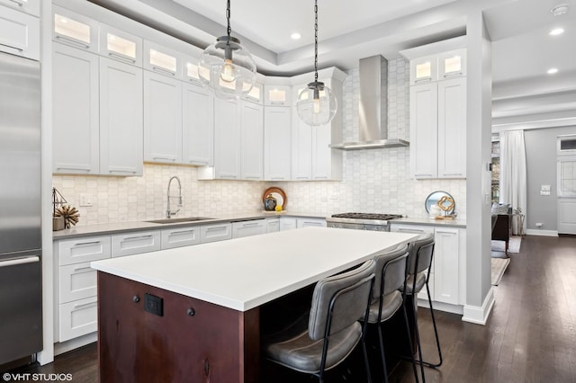 kitchen with dark wood finished floors, a sink, stainless steel appliances, light countertops, and wall chimney exhaust hood