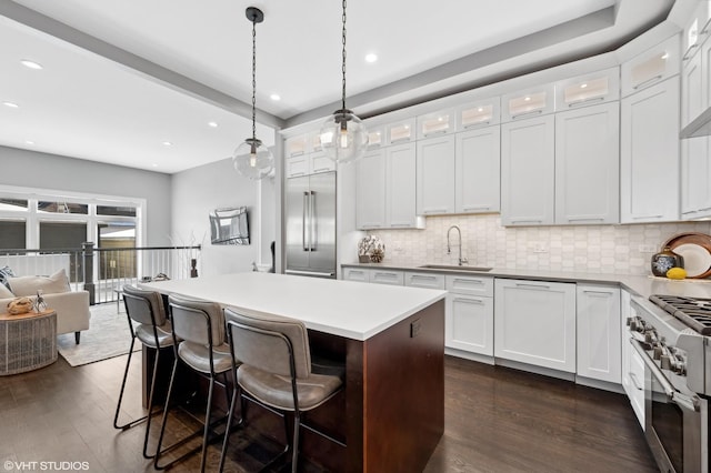 kitchen featuring dark wood finished floors, a sink, high quality appliances, backsplash, and a center island