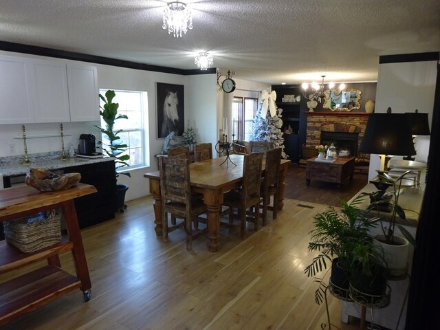 dining room featuring a chandelier, a stone fireplace, a textured ceiling, and light wood-type flooring